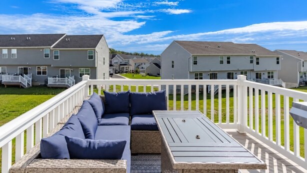 A deck with a sectional sofa and a table, surrounded by a white railing, overlooking a row of townhouses.