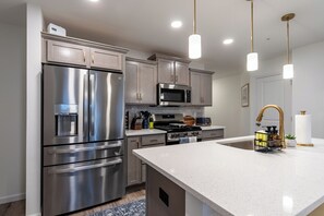 A modern kitchen with stainless steel appliances, a central island, and pendant lighting.
