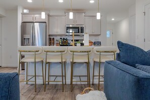 Una cocina moderna con electrodomésticos de acero inoxidable, una barra con taburetes y una sala de estar con sofás.