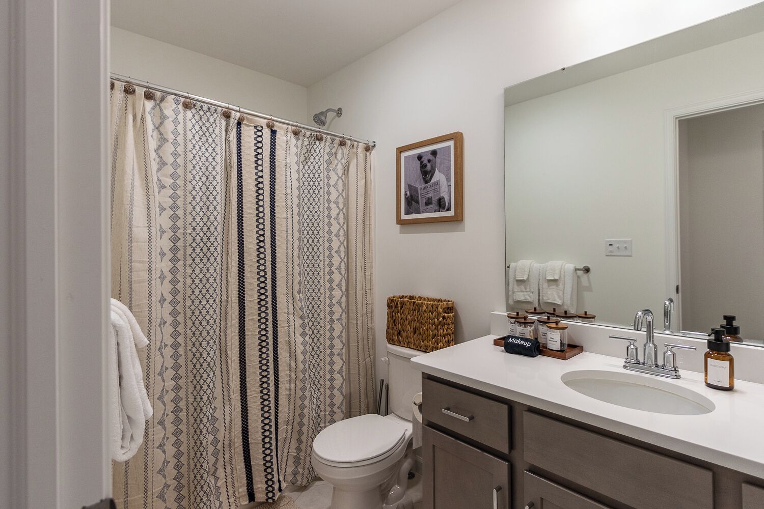 Ein Badezimmer mit Duschvorhang, Toilette, Waschbecken, Spiegel und einem gerahmten Bild an der Wand.