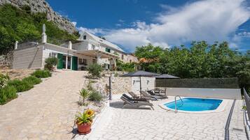 Ein mit Steinplatten belegter Außenbereich mit Swimmingpool, Liegestühlen und einem Haus mit Balkon.