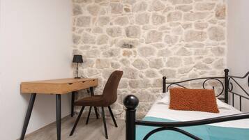 Ein Schlafzimmer mit einer Steinwand, einem Holztisch, einem braunen Stuhl, einem Bett mit blauer Matratze und einem schwarzen Metall-Kopfende.