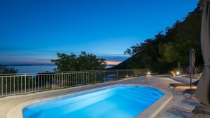 A swimming pool with a view of the sunset, a fenced area, and lounge chairs. - Sea View Villa in Jesenice with Jacuzzi (Jesenice)