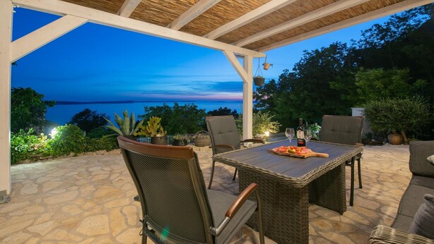 An outdoor patio with a table and chairs, a hanging plant, and a view of the sea. - Sea View Villa in Jesenice with Jacuzzi (Jesenice)