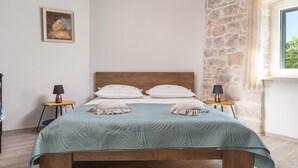 A bedroom with a stone wall, a wooden bed, and a window with a view. - Sea View Villa in Jesenice with Jacuzzi (Jesenice)
