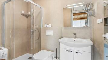 A bathroom with a glass-enclosed shower, a white toilet, a sink with a mirror, and a towel rack.