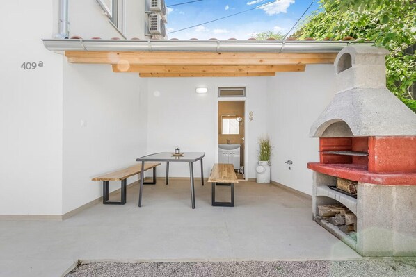 A modern outdoor patio with a wooden bench, a table, and a stone-built barbecue grill.