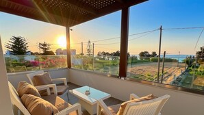 Un balcone con mobili in vimini, un tavolino in vetro e vista sul tramonto sul mare.