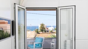 Un balcón con una silla blanca y un farol, con vistas a una playa y edificios.