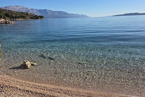 Ein klarer See mit steiniger Uferlinie und Bergen im Hintergrund.