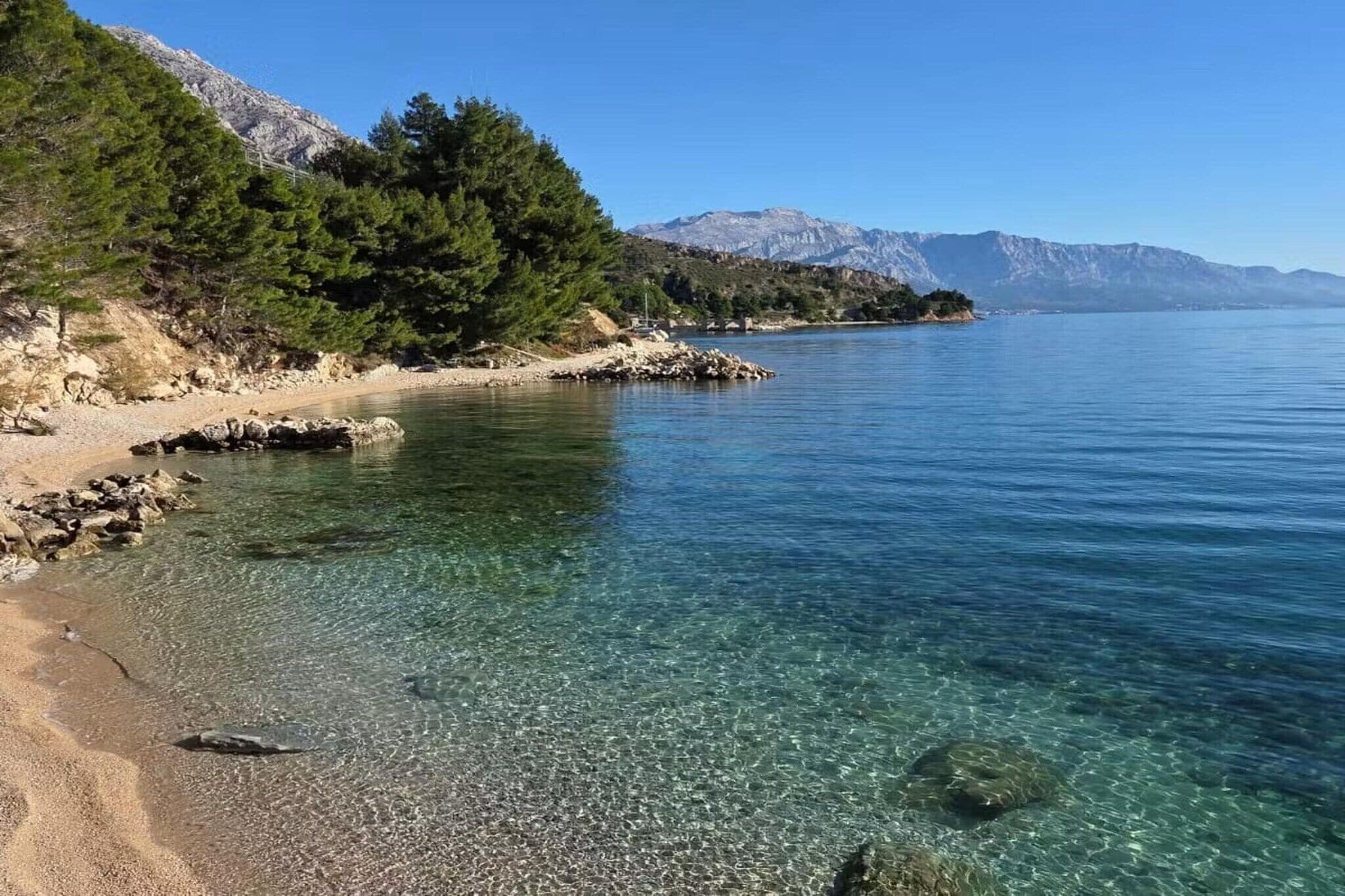 En klar sjö med en stenig strand, omgiven av träd och berg.