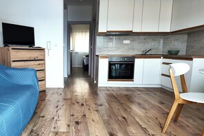 A modern kitchen with white cabinets, a built-in oven, and a wooden dining table with a chair. - Seaside apartment in Lokva Rogoznica (Lokva Rogoznica)