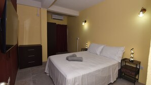 A hotel room with a bed, a dresser, a mirror, a TV, and a wall-mounted light fixture. - Spacious 3-bedroom apartment in adorable Gros Islet with AC near popular spots (Gros Islet)