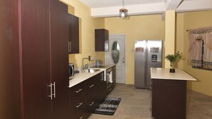 A kitchen with dark wooden cabinets, a stainless steel refrigerator, and a tiled floor. - Spacious 3-bedroom apartment in adorable Gros Islet with AC near popular spots (Gros Islet)