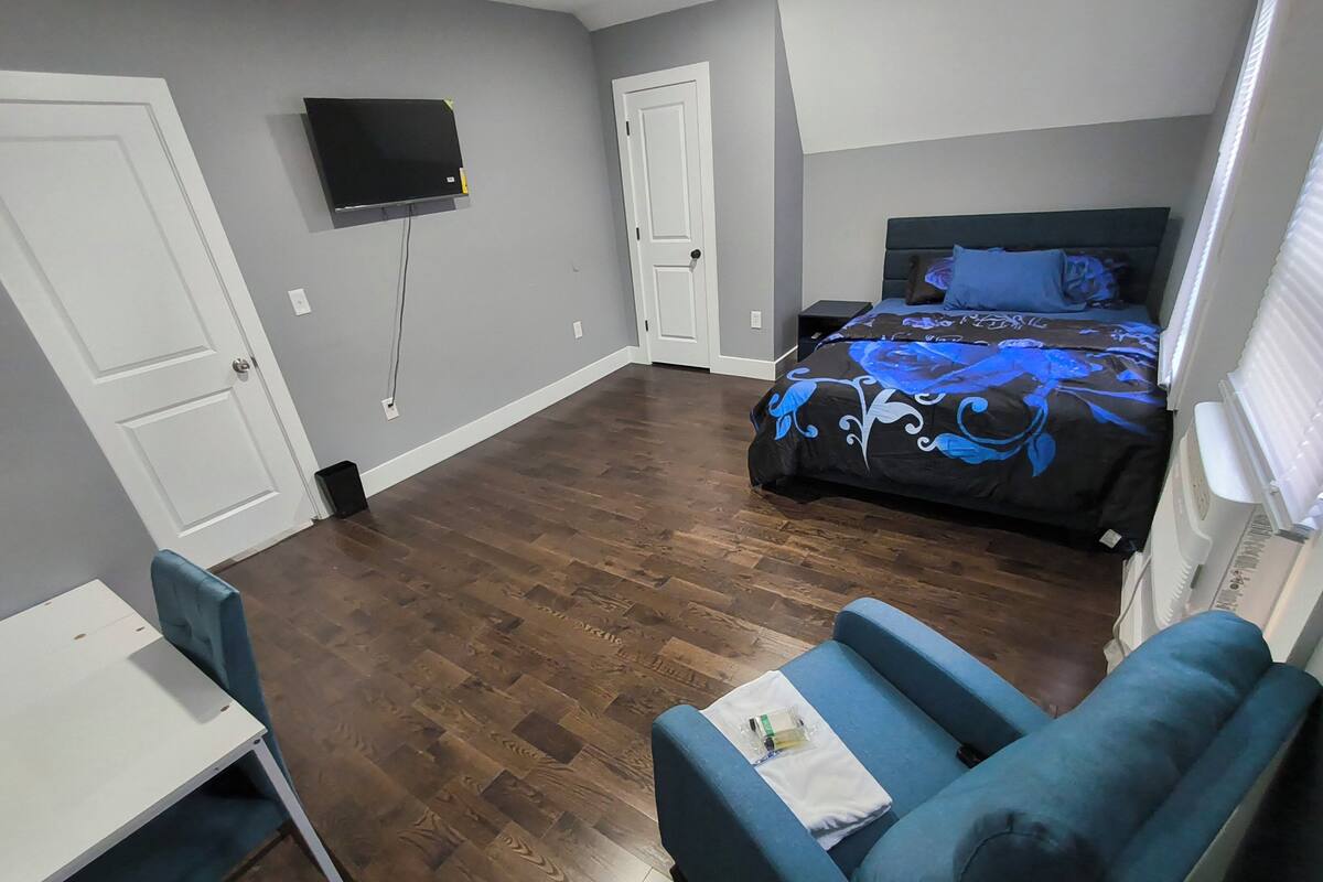 Una habitación con cama, escritorio, silla y televisor montado en la pared.