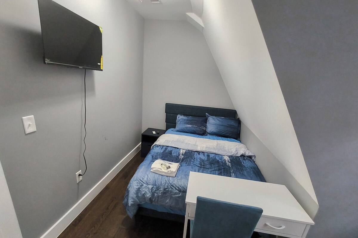 Un dormitorio pequeño y moderno con una cama, un escritorio y una televisión montada en la pared.