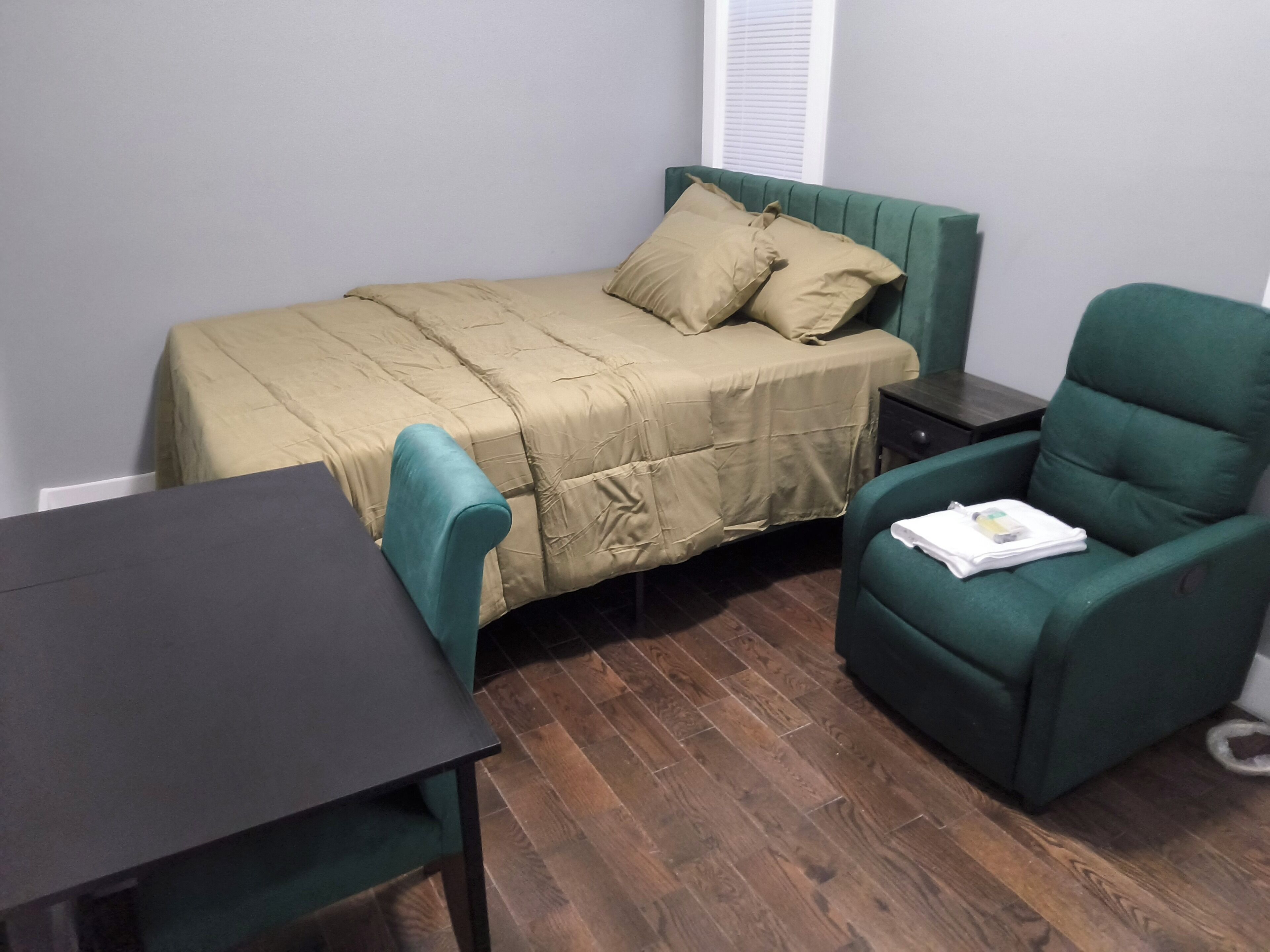 Une petite pièce comprenant un lit, une chaise, une table et une table de chevet.