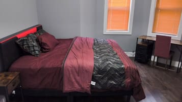 Een slaapkamer met een bed, een bureau en twee ramen.