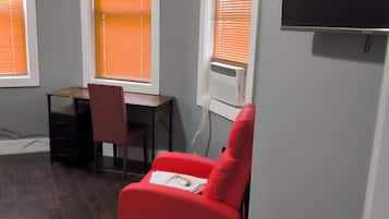 Une pièce avec une chaise rouge, un bureau et un téléviseur fixé au mur.