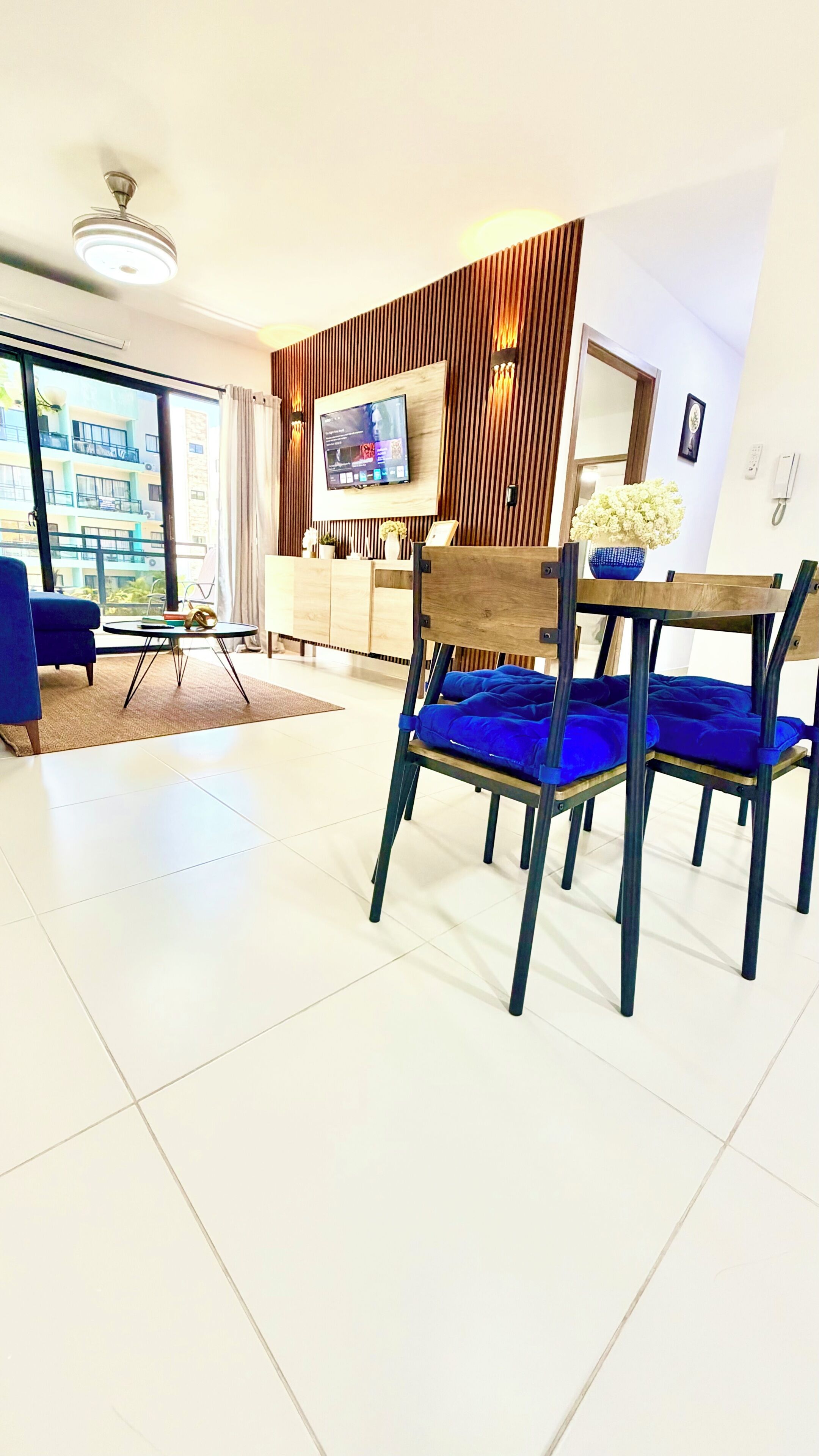 Una sala de estar moderna con un televisor, sillones azules, un sofá y vistas a un edificio.