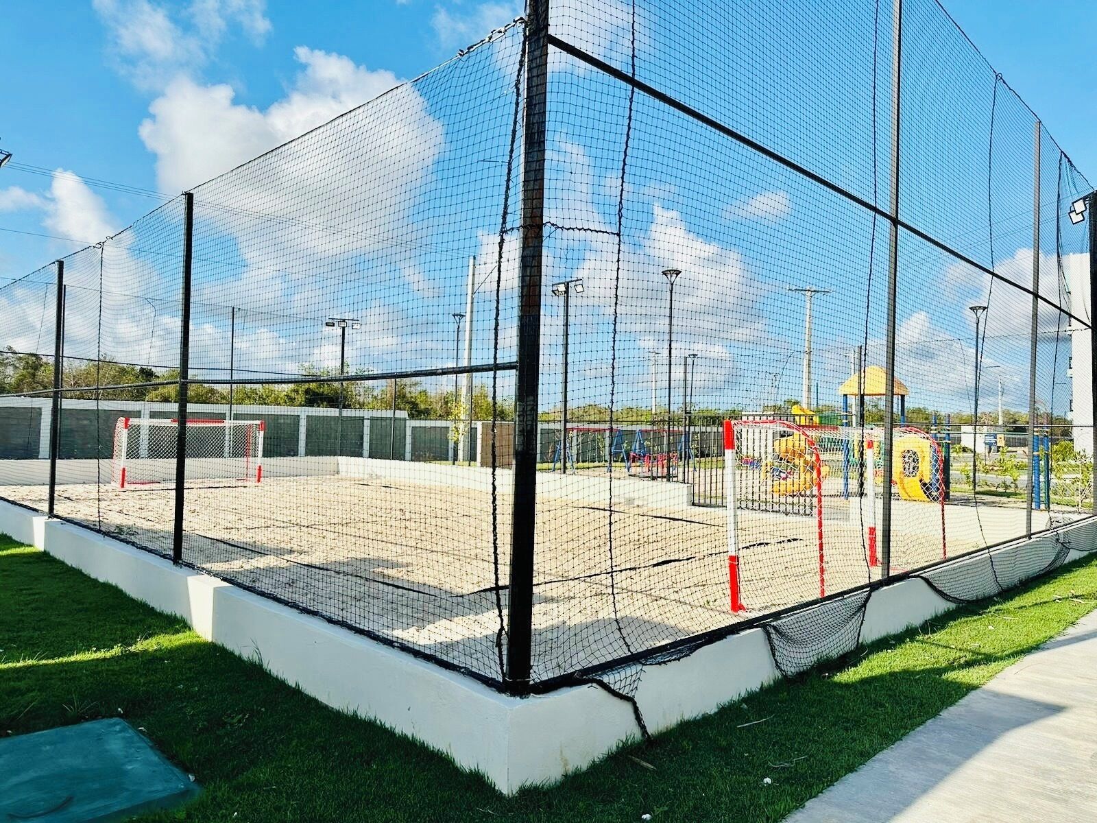 En sportspark omkranset af nettinghegn med målstolpe og legeplads i baggrunden.