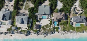 A coastal residential area with multiple houses, some with swimming pools, and a beach in the foreground. - Greystone Villa: 7-Bedroom Oceanfront Luxury on a Private Exuma Beach (Forbes Hill)
