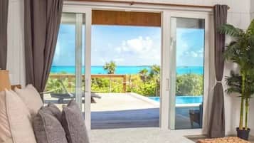 A room with a view of the ocean, a sliding glass door, a bed with pillows, and a potted plant.