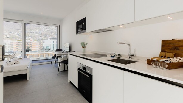 A modern kitchen with a large window, a dining area, and a bed. - {Suite 508} Gym, Business Room, Modern, Relax (Lugano)