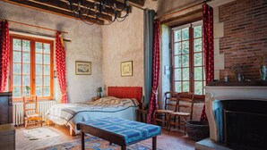 Ein traditionell eingerichteter Raum mit Bett, einer Bank, einem Kamin und einem Fenster mit Vorhängen.
