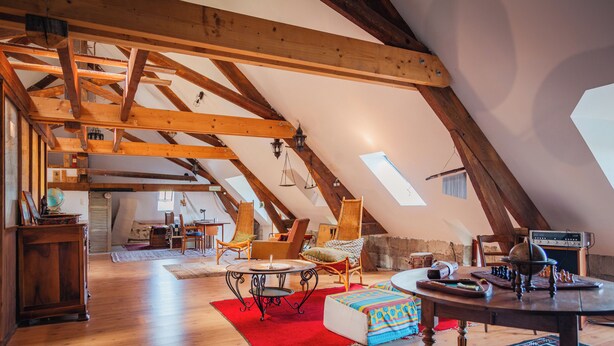 Ein Dachzimmer mit freiliegenden Holzbalken, einem roten Teppich, einem runden Tisch und einem Sofa.