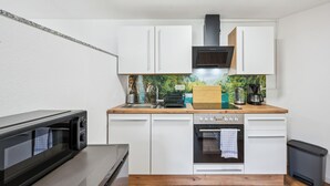 Une cuisine compacte avec des meubles blancs, un four à micro-ondes, une cuisinière et une machine à café.