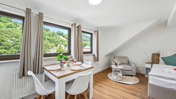 Une pièce moderne et bien éclairée, comprenant un coin repas, un lit et offrant une vue sur la verdure environnante.