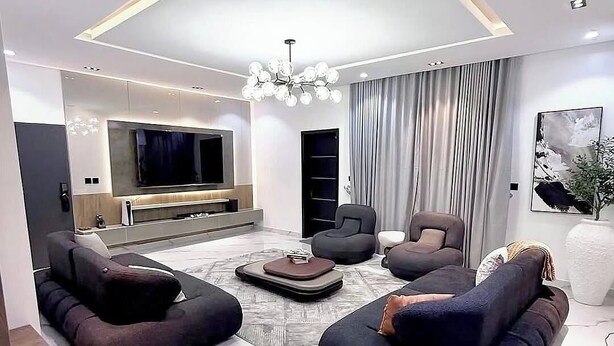 A modern living room with a large TV, dark sofas, and a chandelier. - 501 Aparthotel (Akure)
