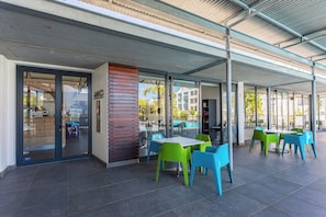 An outdoor café with a covered seating area, glass doors, and a pool visible through the windows. - Modern 3-Bed Garden Pool Gym by CTHA (Cape Town)