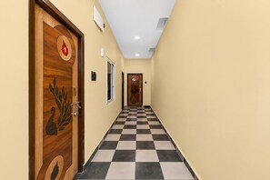 A hotel hallway with checkered flooring, wooden doors with decorative designs, and a light-colored wall. - Classic Sri Jogulamba Residency (Balanagar)