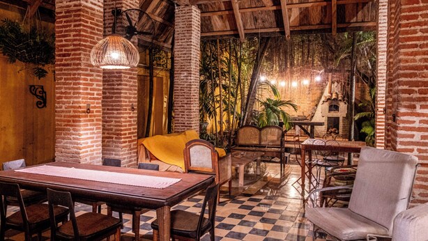 A dining area with a checkered floor, wooden furniture, and a brick wall. - CASA DE COLUMNAS (Cartagena)
