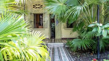 A building with a tiled entrance, surrounded by lush greenery and palm trees.