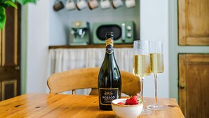 Una botella de vino Nozeco, dos copas de vino blanco, un bol de fresas y una mesa de madera en una cocina.