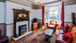 Una habitación con chimenea, un sofá, una mesa y un ventanal con cortinas.