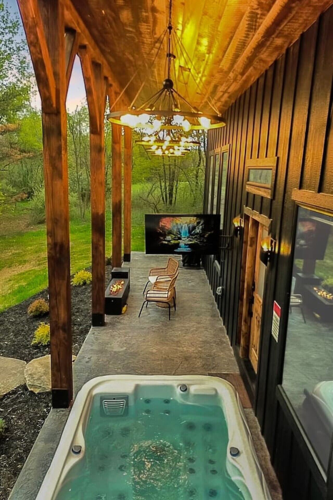 Un espace extérieur abrité comprenant un jacuzzi, une terrasse en bois et un coin salon offrant une vue sur une cascade.