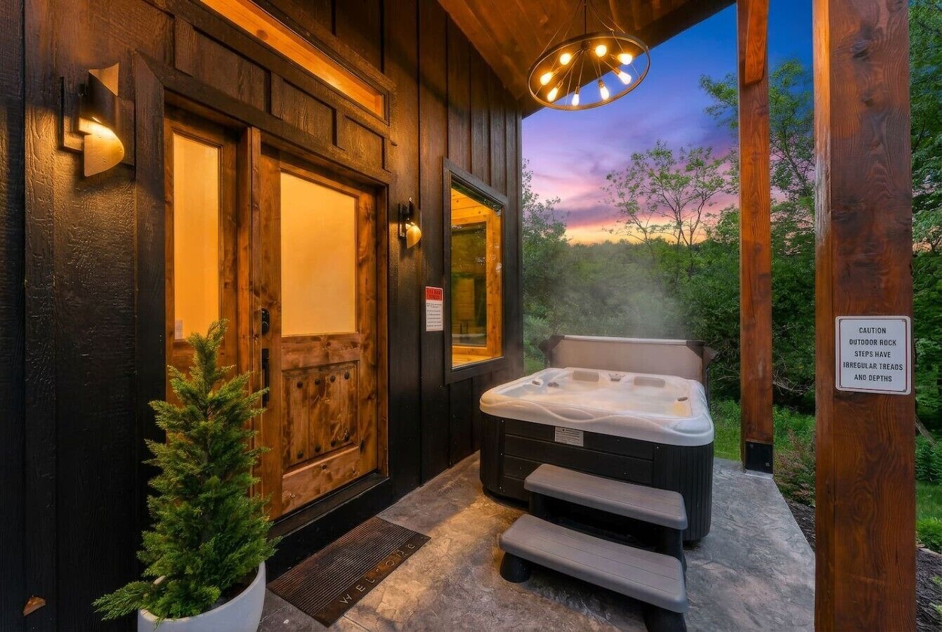 A wooden spa building with a hot tub, a welcome mat, and a caution sign about outdoor rock steps.