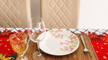 Una mesa de comedor con un plato floral, dos copas de vino y cubiertos sobre un mantel rojo con diseño de rombos.