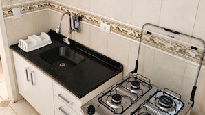 A compact kitchen with a gas stove, a sink, and white cabinets. - Apto Rodoviária e Mercado Municipal (Curitiba)