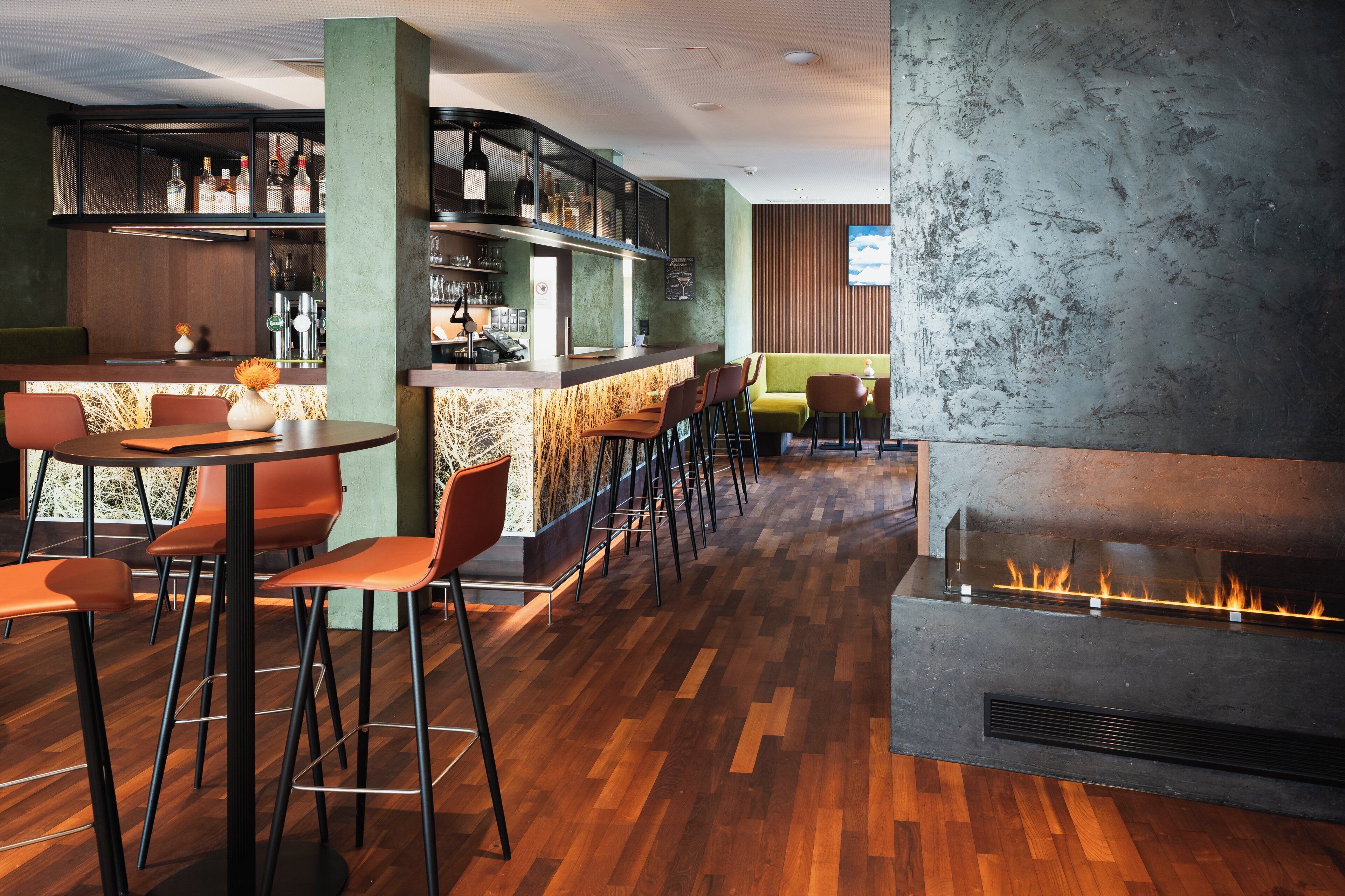 Eine Bar mit einer langen Theke, Hockern und einem Kamin.