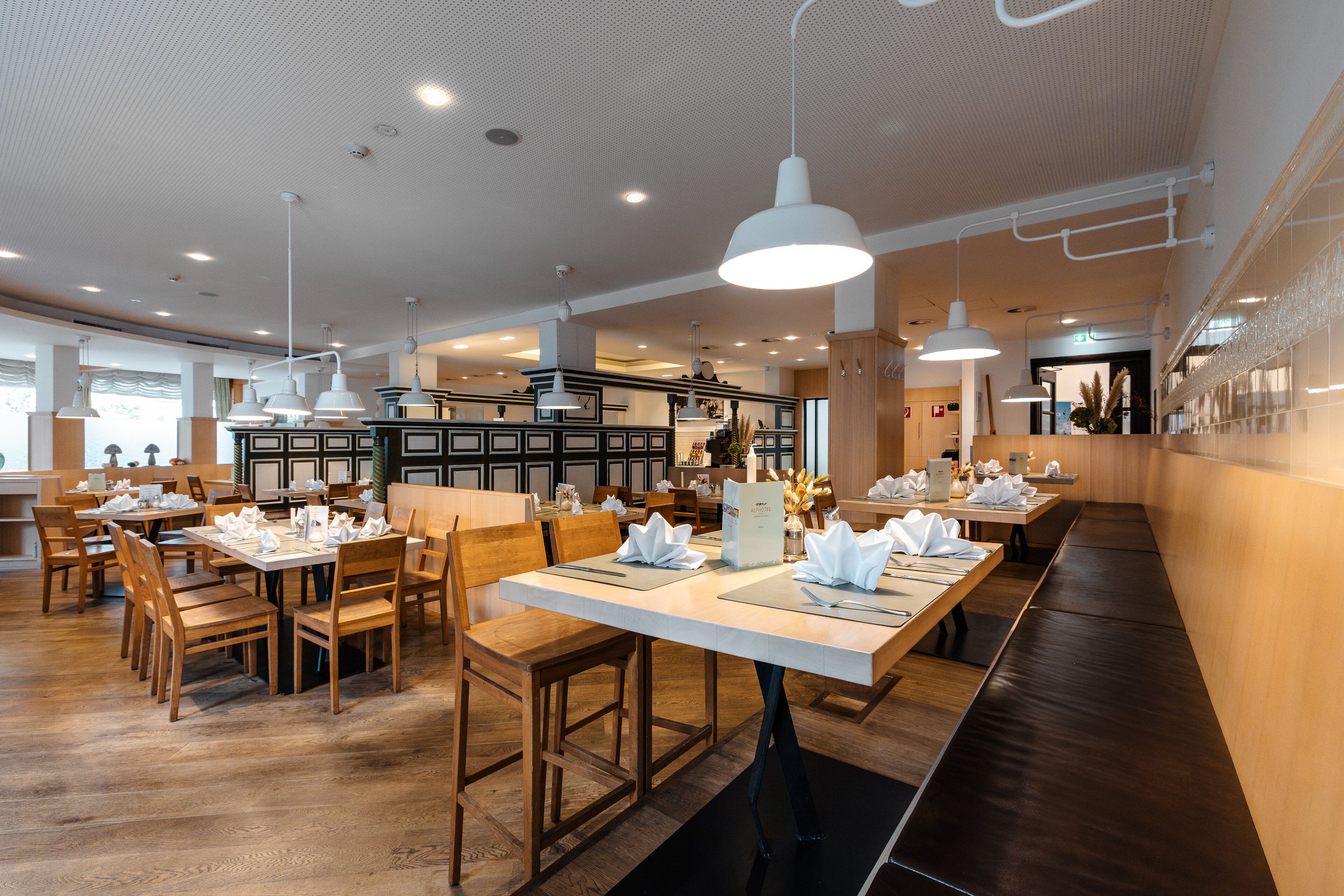 Ein Restaurant mit Holztischen und -stühlen, weißen Tischdecken und Pendelleuchten.