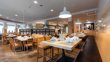 Ein Restaurant mit Holztischen und -stühlen, weißen Tischdecken und Pendelleuchten.