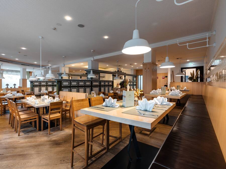 Un restaurante con mesas y sillas de madera, manteles blancos e iluminación colgante.