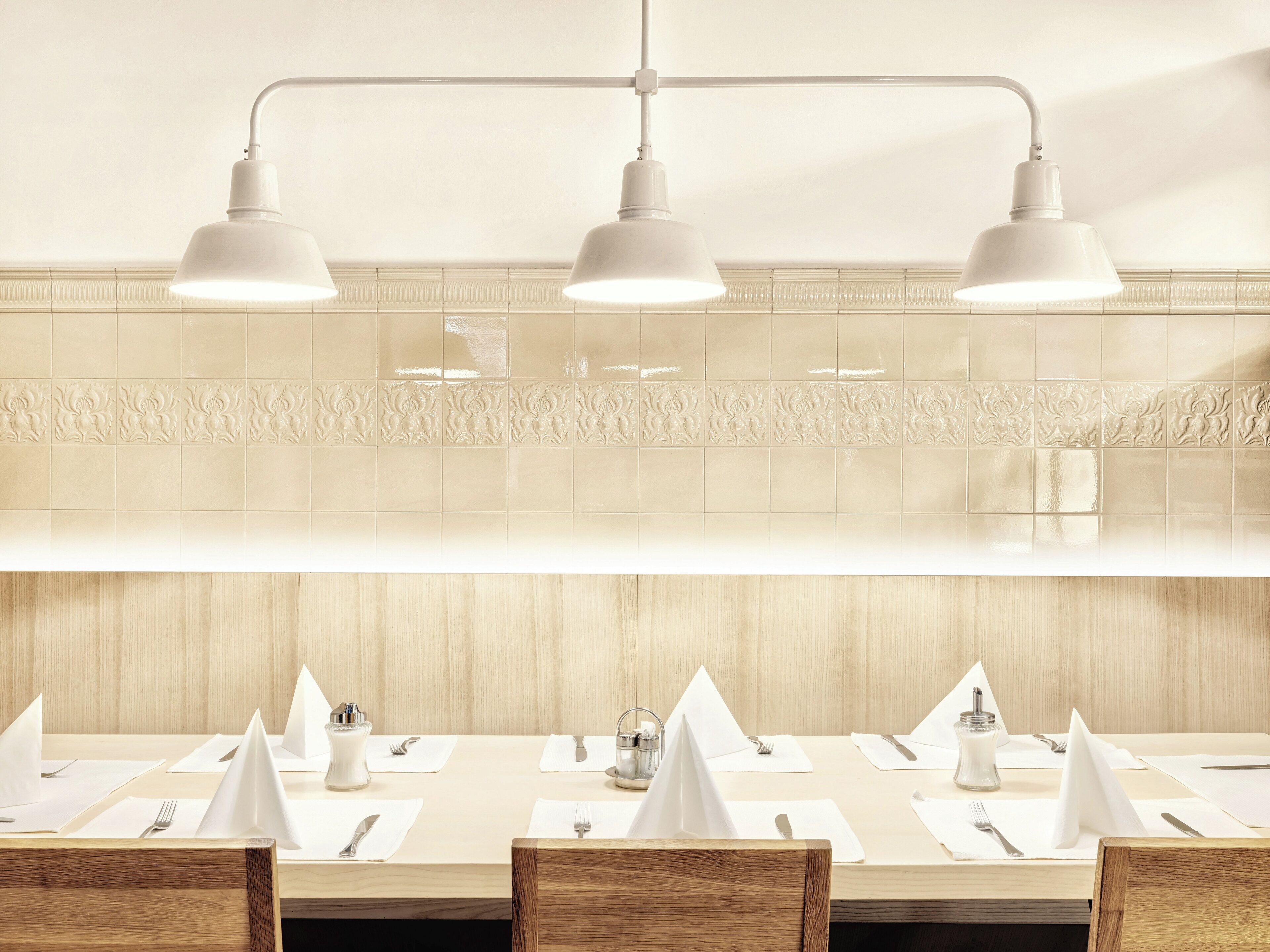 Ein Restaurantinnenraum mit einem langen Esstisch, Pendelleuchten an der Decke und dekorativen Wandfliesen.