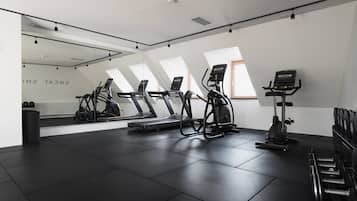 Ein Fitnessraum mit Laufbändern, Crosstrainern und einem Ergometer, ausgestattet mit einem großen Spiegel und Oberlichtern.