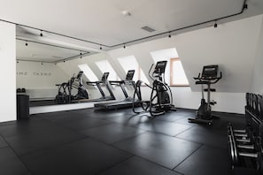 Un gimnasio con cintas de correr, elíptica y bicicleta estática, con un espejo grande y tragaluces.